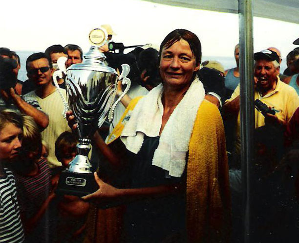 Kirsten Seidel holding a large trophy with people gathered behind her.
