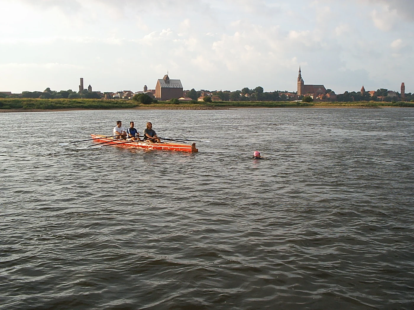 Swimmer and a red support canoe on the Elbe, with buildings along the opposite bank